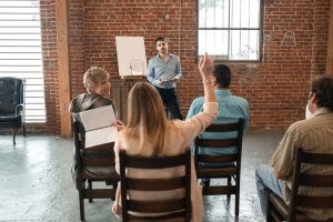 Formateur animant une session devant un petit groupe d'adultes dont une participante lève la main, illustrant une formation Qualiopi