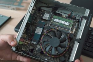 Mini-PC ouvert tenu en main, carte mère et ventilateur visibles, serveur compact pour faire tourner des modèles de décision en local